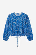 A blue long-sleeve crop top with a white block print pattern, featuring a drawstring tie at the hem and elasticized cuffs, shown against a plain light gray background.